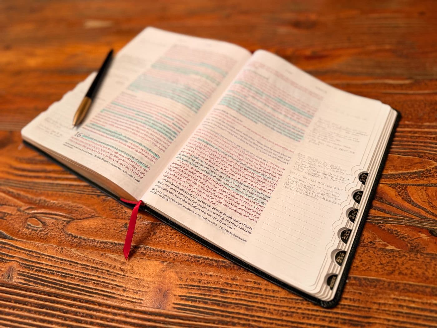 An open Bible on a wooden table, marked up with highlighter and handwritten notes