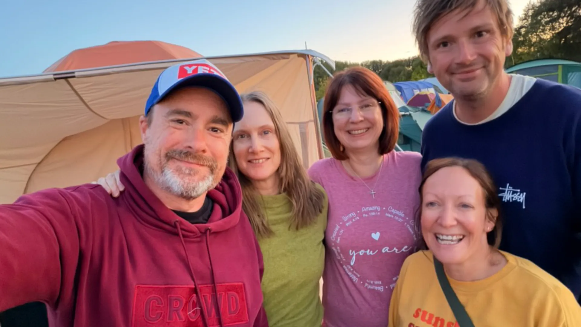 Five members of Crowd Church standing arm-in-arm outside a tent at Wildfires as the sun goes down